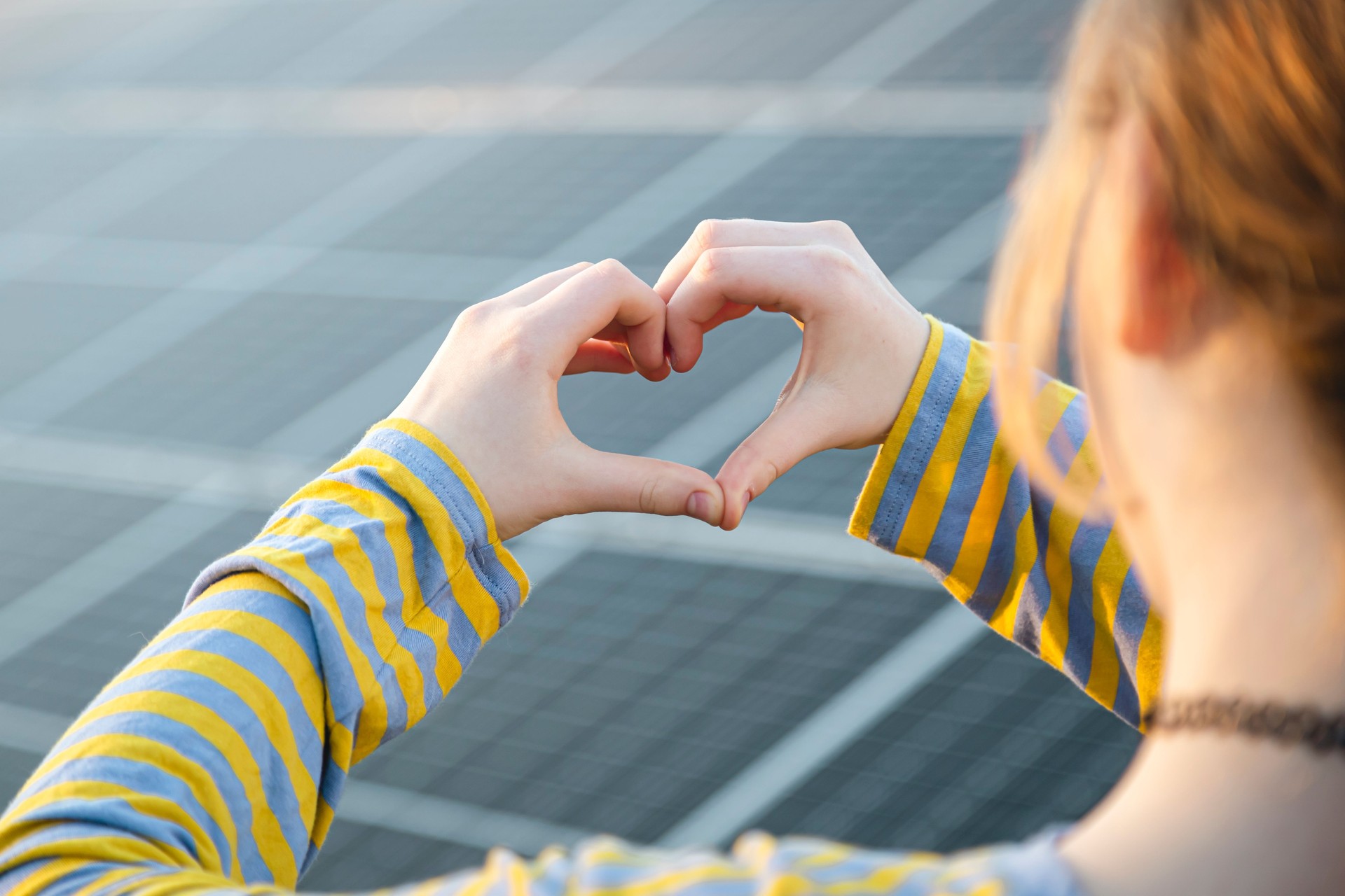Ragazza che sta vicino ai pannelli solari e mostra il simbolo del cuore, concetto di energia solare.